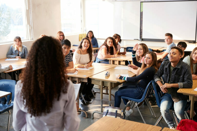 rear view of female high school teacher standing at front of class teaching lesson